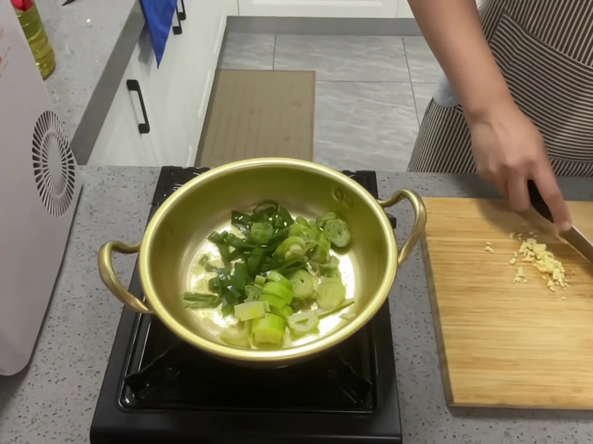 기름을 두른 황금빛 냄비에서 대파와 마늘을 볶는 모습.