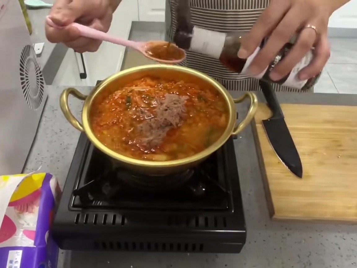끓고 있는 붉은 참치 김치찌개에 짙은 색의 액젓(또는 국간장) 한 숟가락을 붓는 모습.