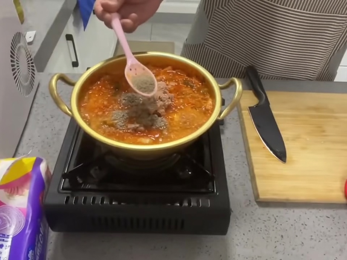 붉은 참치 김치찌개 냄비에 숟가락으로 소고기 다시다 가루를 뿌리는 모습.