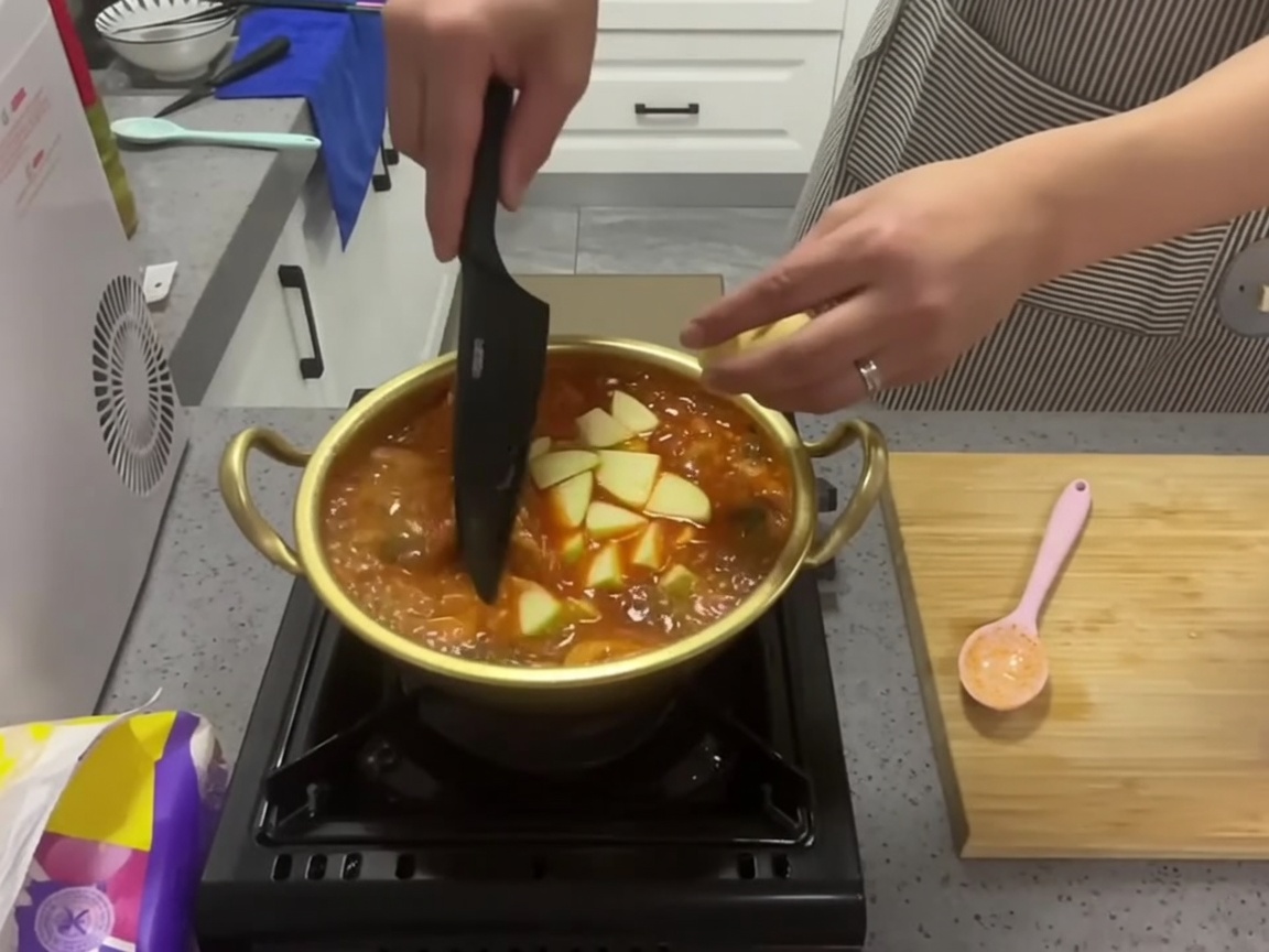 끓고 있는 붉은 김치찌개 냄비에 신선한 녹색 애호박 슬라이스를 넣는 모습.