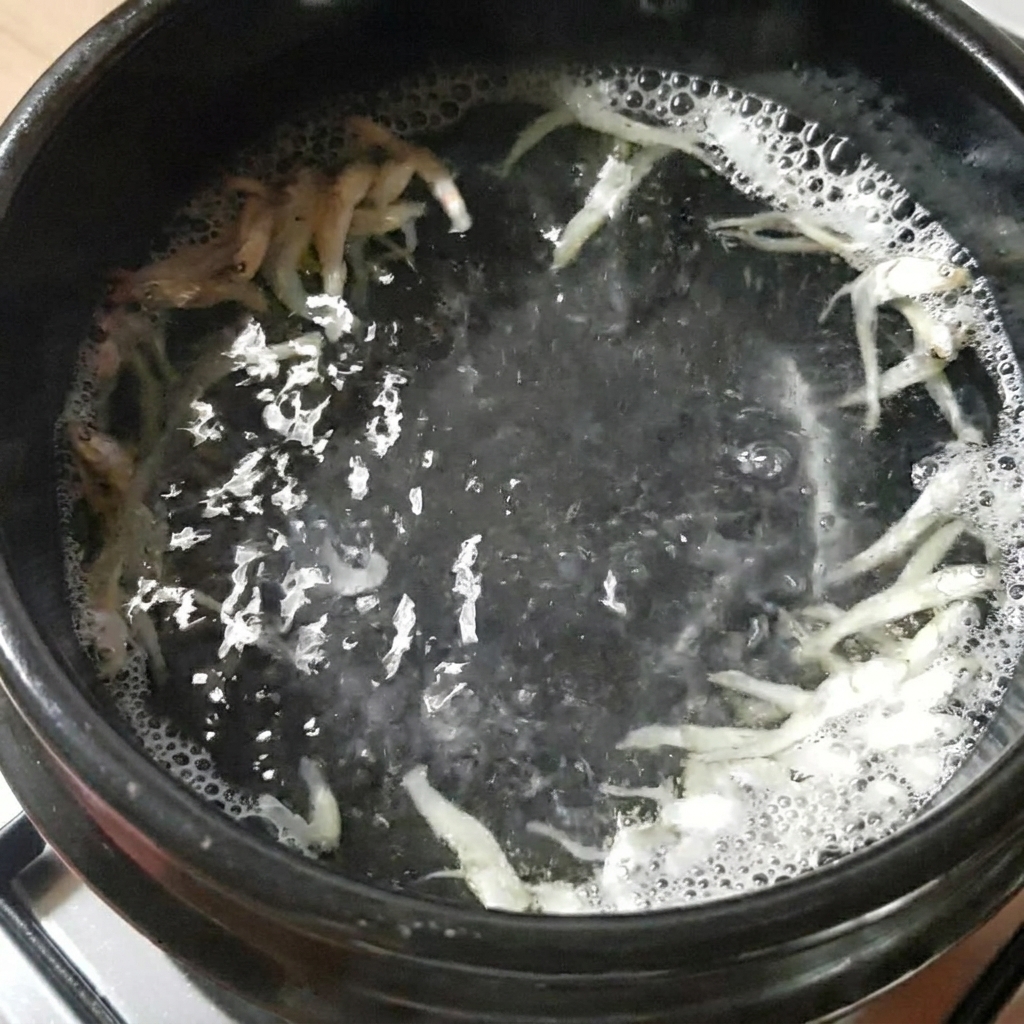 가스레인지 위에서 물, 건멸치, 다시마가 들어 있는 뚝배기가 끓고 있는 모습.