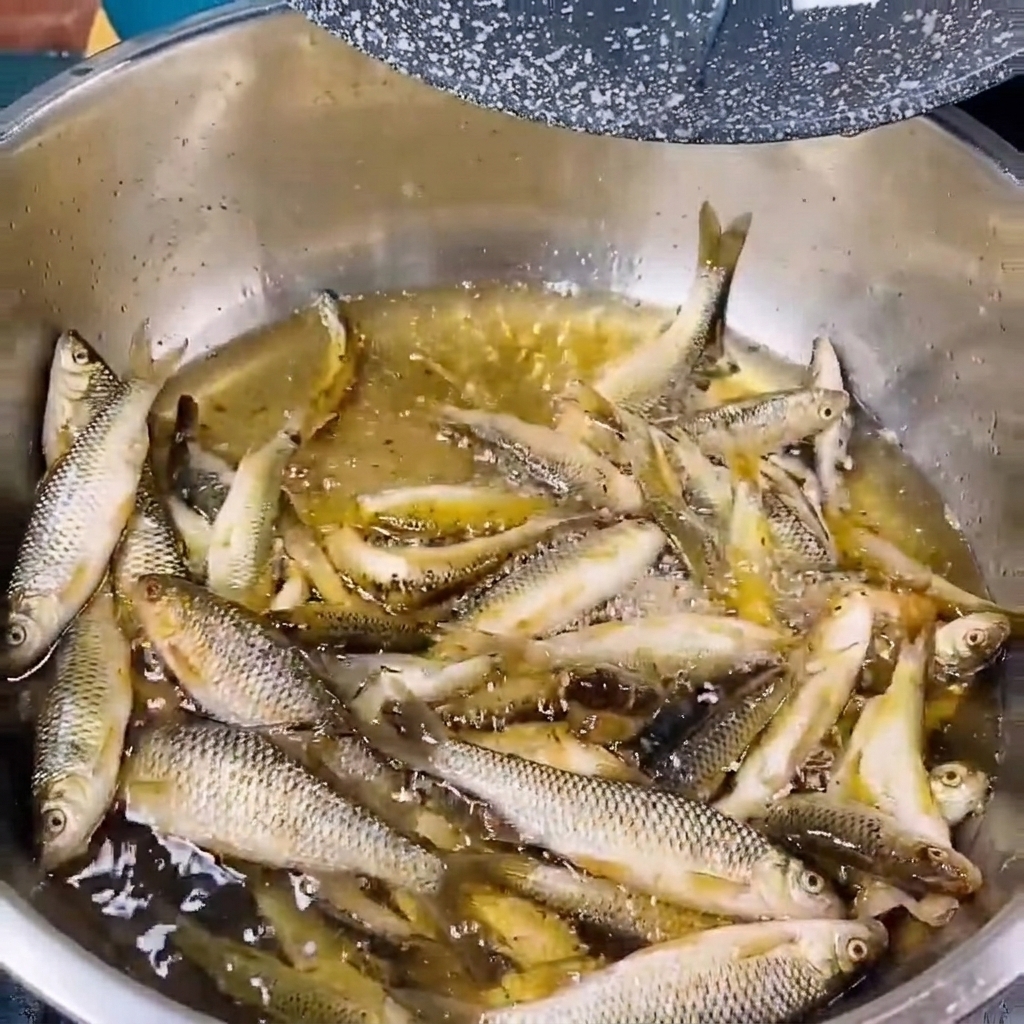 투명한 물이 담긴 금속 그릇에 작은 민물고기를 헹구는 모습.