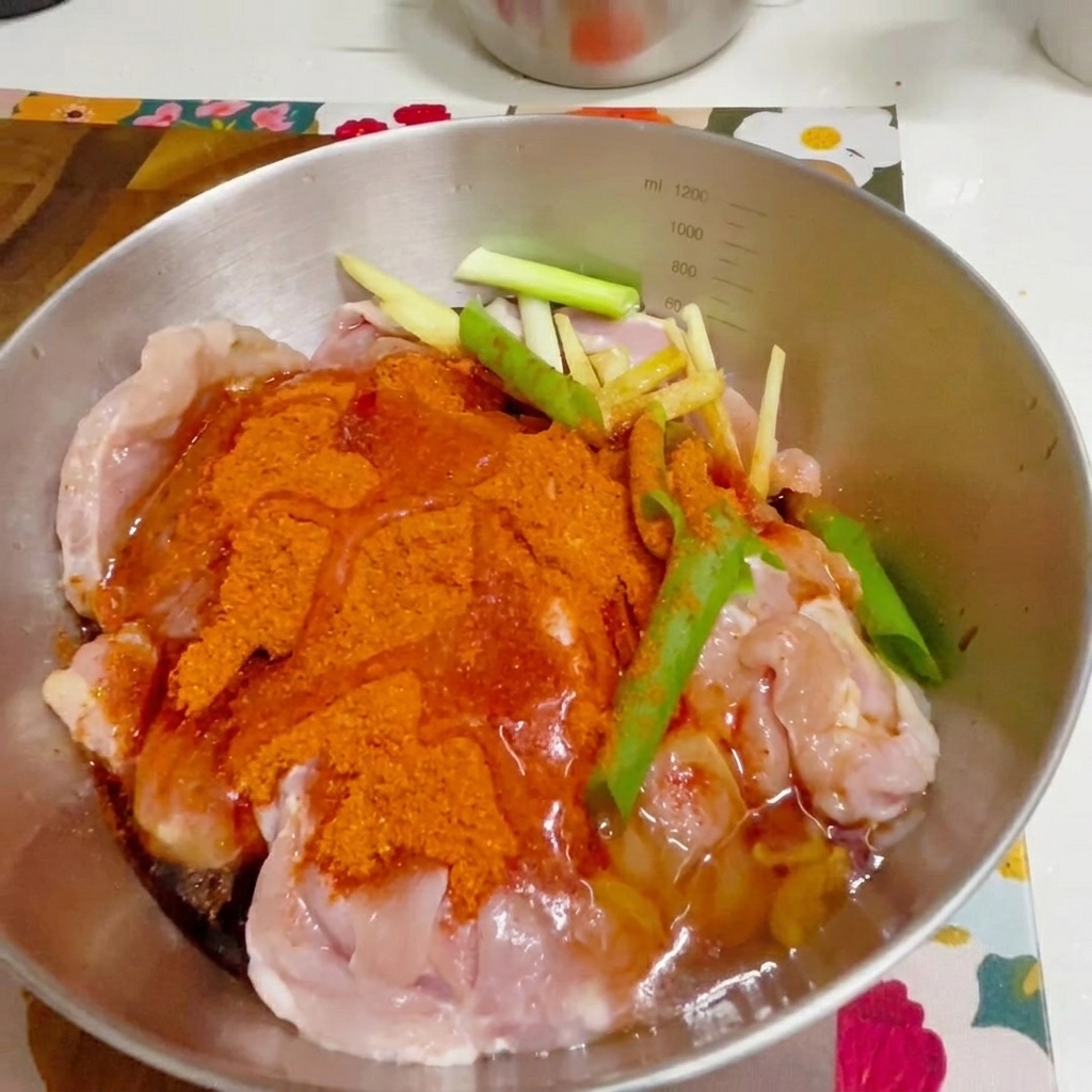 장갑을 낀 손으로 볼 안의 양념된 치킨을 섞는 모습.