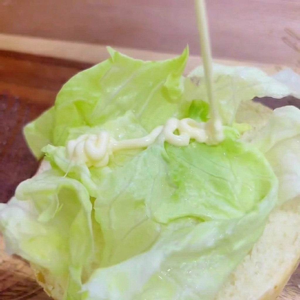 빵 위에 올려진 양상추 위로 마요네즈를 지그재그로 뿌리는 모습.
