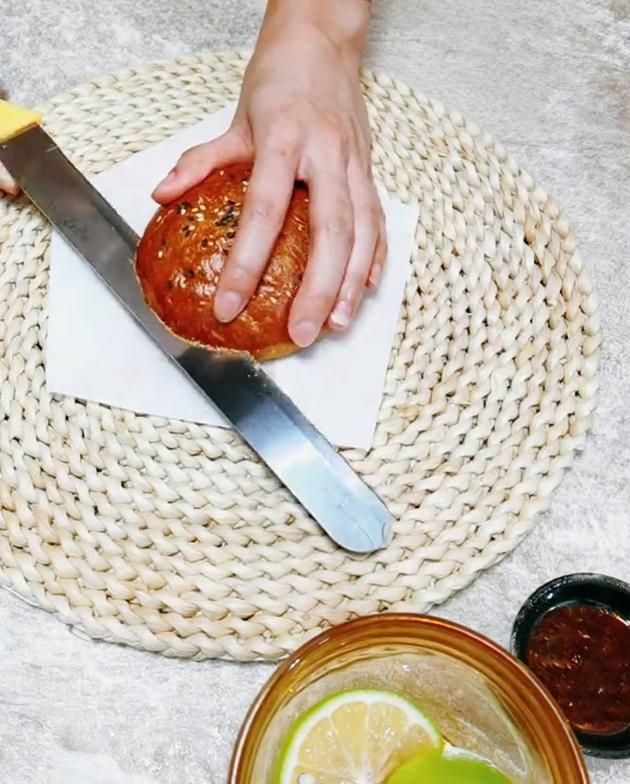 도마 위에서 빵칼을 이용해 수제 버거 번을 반으로 자르는 모습.