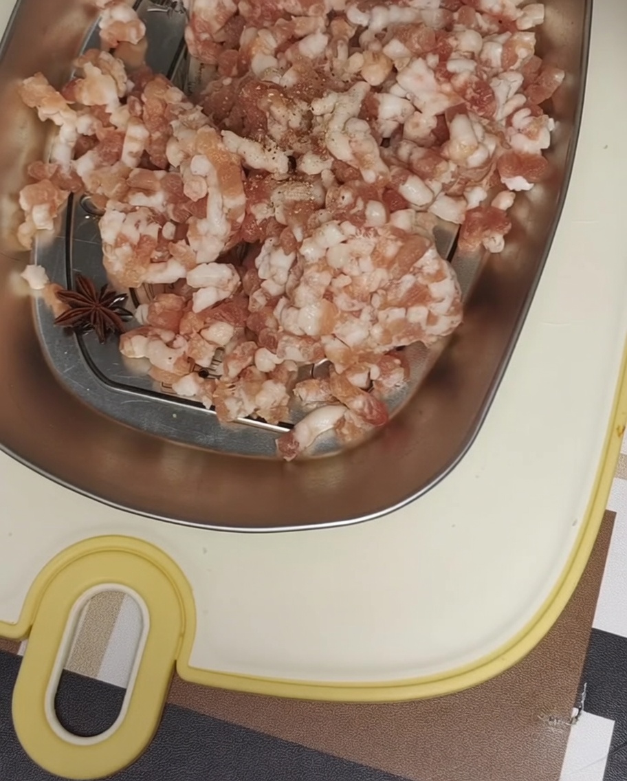 금속 쟁반에 담긴 다진 돼지고기에 후추와 바다 소금을 뿌리는 모습.