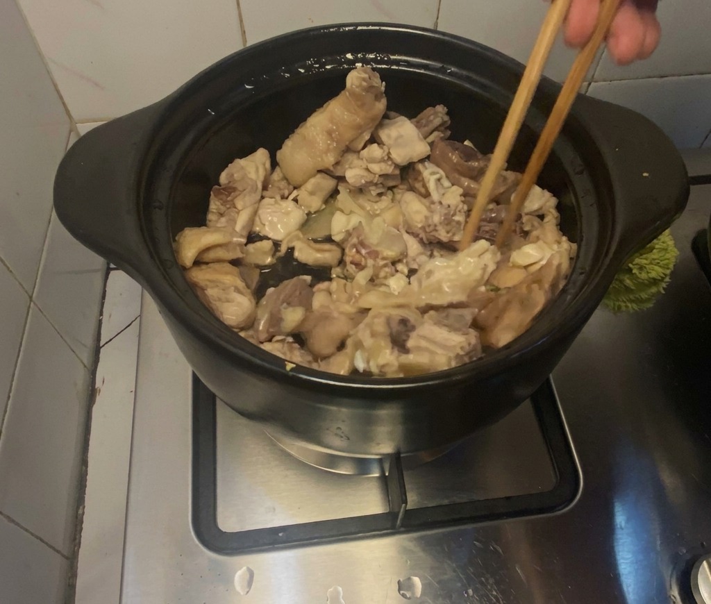 가스레인지 위에 놓인 검은 뚝배기 안에서 나무 젓가락으로 닭고기를 볶고 있는 모습.