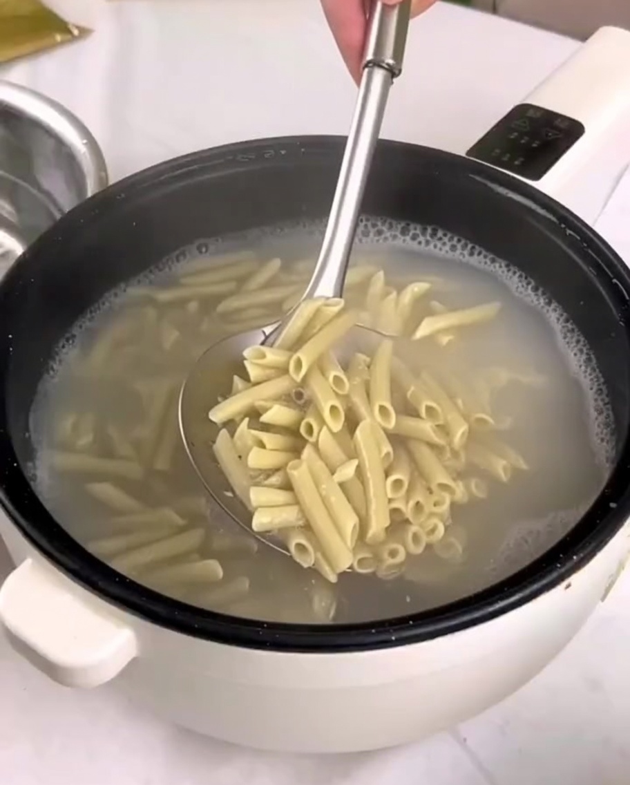 삶은 펜네 파스타를 구멍 뚫린 숟가락을 사용해 냄비에서 찬물이 담긴 그릇으로 옮기는 모습.