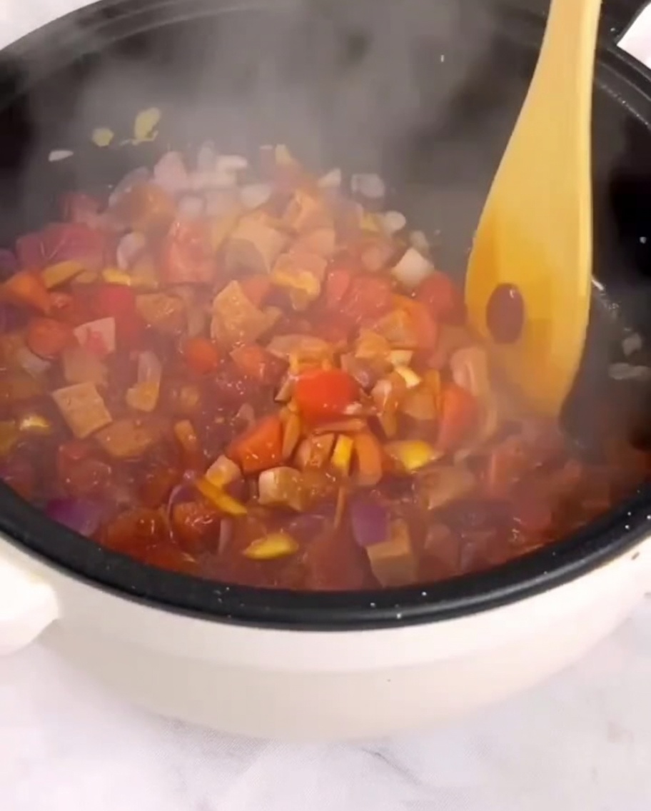 나무 주걱으로 팬에 다진 토마토, 햄, 채소를 볶고 있는 모습.