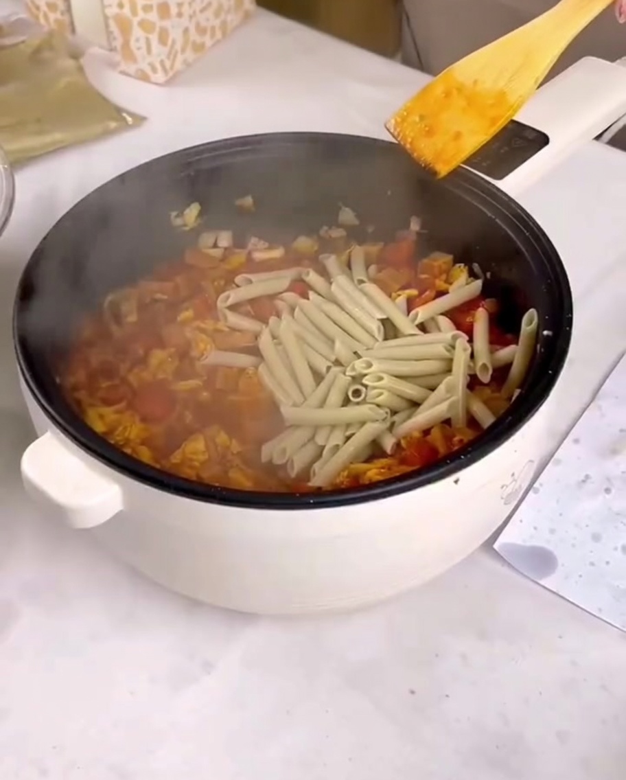소스와 볶은 재료가 있는 팬에 삶은 펜네 파스타를 더하는 모습.
