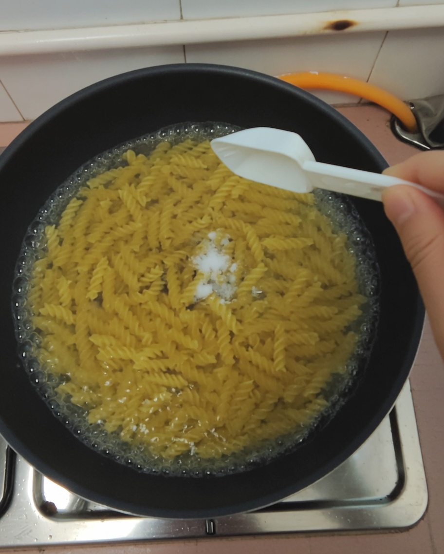 끓는 파스타 냄비에 소금 한 숟가락을 넣는 모습.