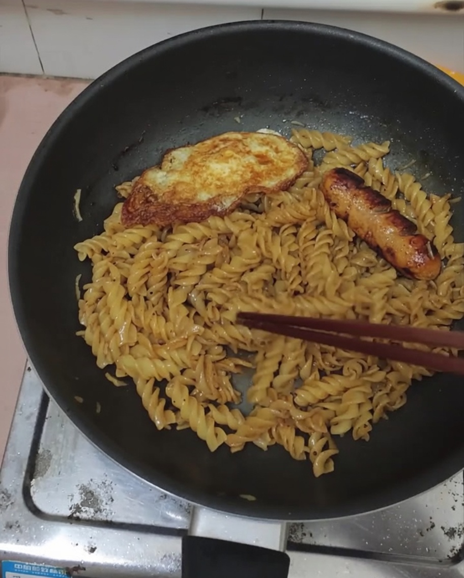 양념된 블랙 페퍼 푸실리 팬 위에 올려진 계란 프라이와 소시지.