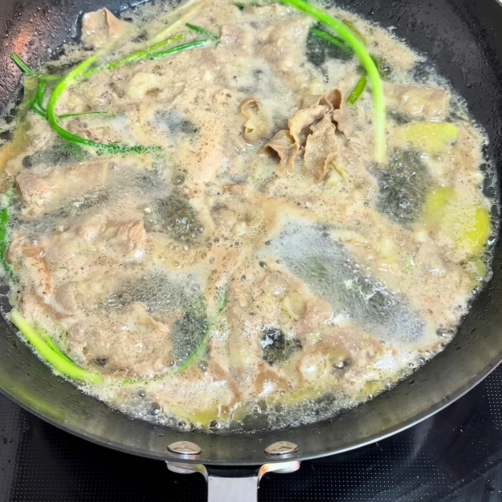 끓는 물이 담긴 팬에 얇게 썬 소고기와 신선한 쪽파를 데치는 모습.