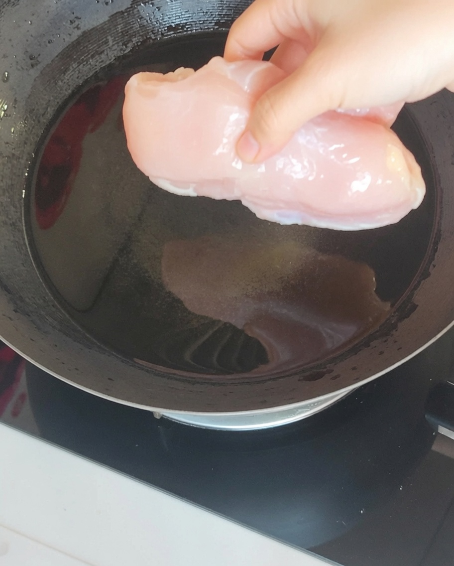 웍에 끓는 물을 넣고 생강, 대파와 함께 닭가슴살을 데치는 모습.