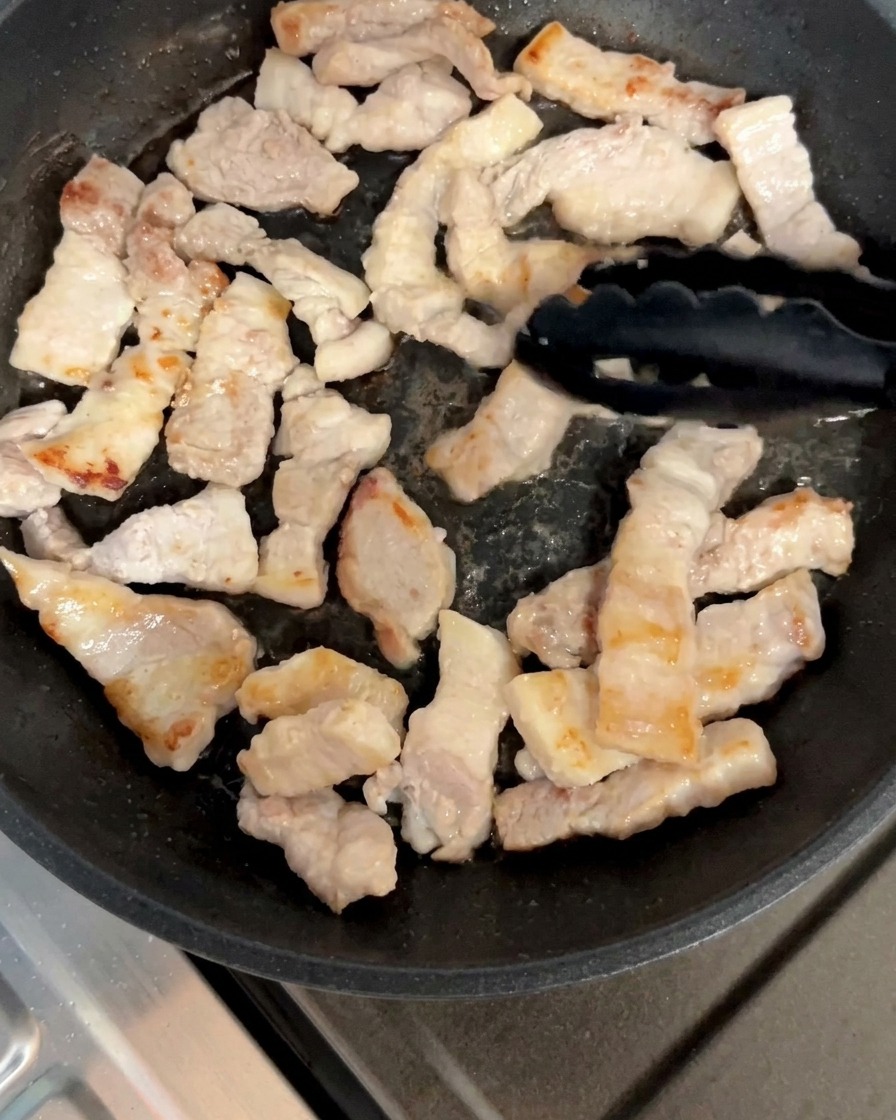 삼겹살 조각들을 팬에서 노릇해질 때까지 뒤집으며 굽는 모습.