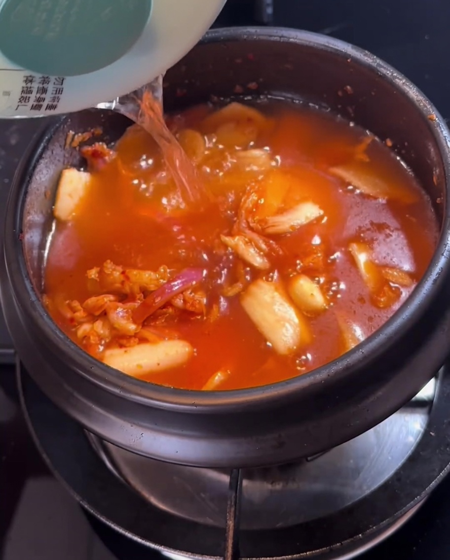 볶은 재료가 담긴 뚝배기에 물을 붓는 모습.