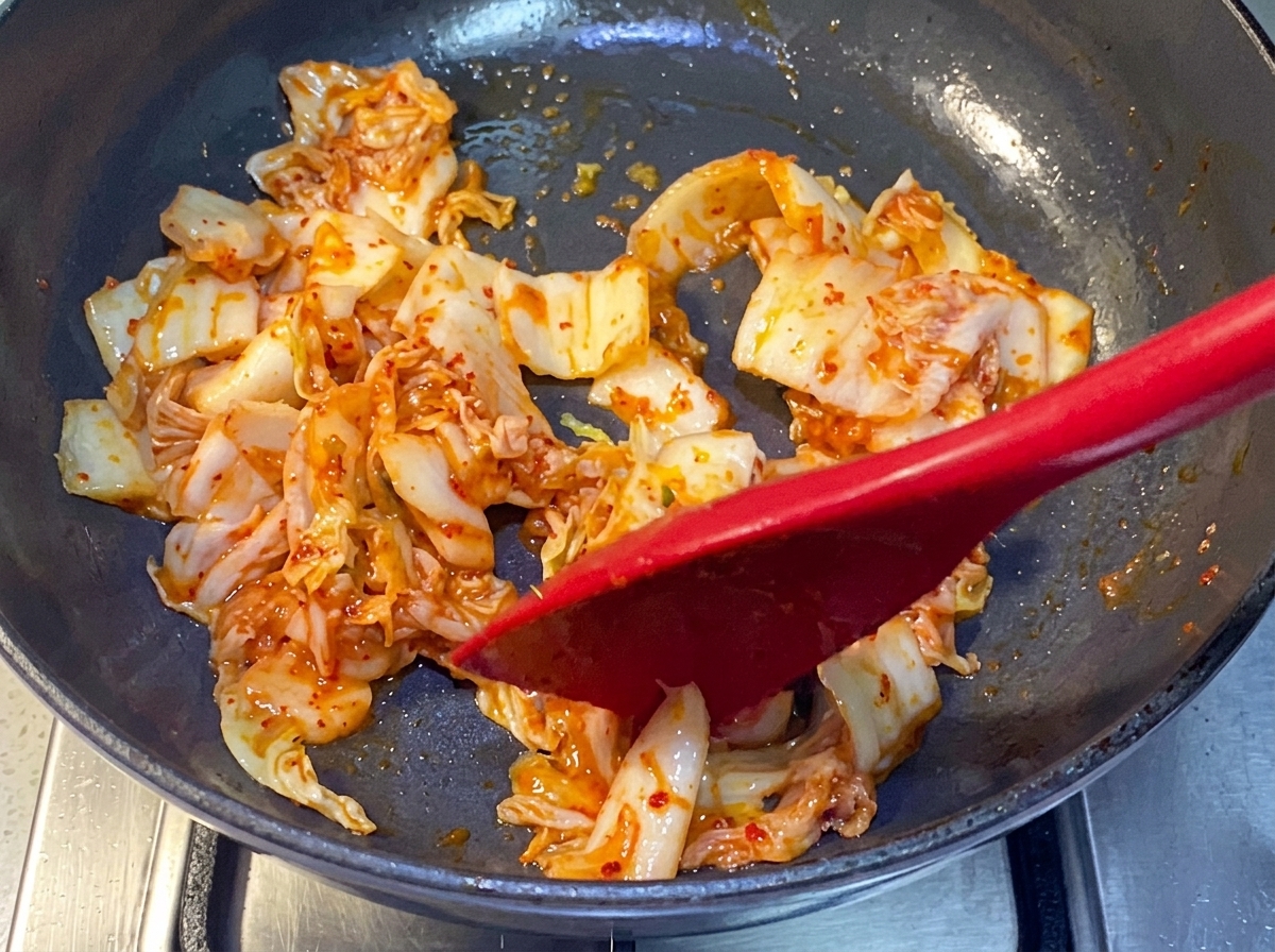 빨간색 실리콘 주걱으로 팬에서 김치를 볶는 모습.