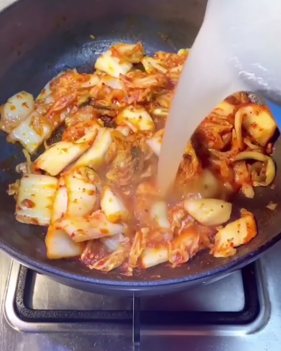 잘 볶아진 김치가 있는 팬에 돼지갈비 육수를 붓는 모습.