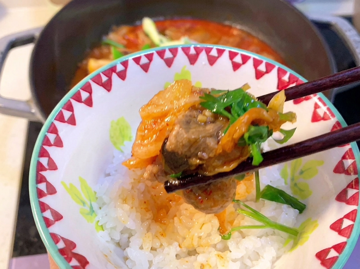 보글보글 끓는 김치와 돼지갈비 찌개에 숟가락으로 고추장을 저어 섞는 클로즈업 뷰.