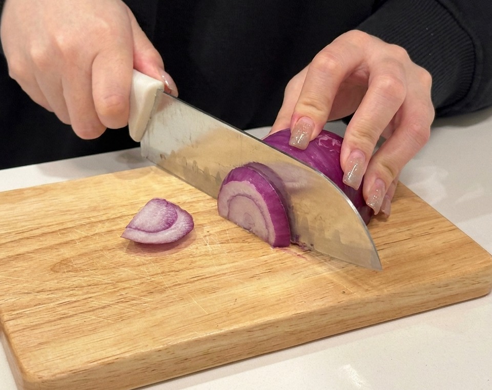 나무 도마 위에서 적양파를 채 써는 모습.
