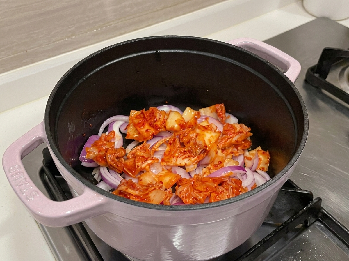 냄비 안에서 붉은 김치와 양파가 함께 볶아지며 맛있는 즙이 나오는 모습.