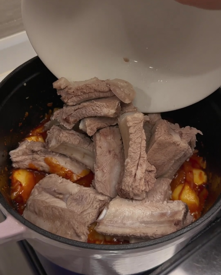 양념된 김치 베이스가 있는 냄비에 미리 데쳐둔 돼지갈비를 흰 그릇에서 옮겨 담는 모습.