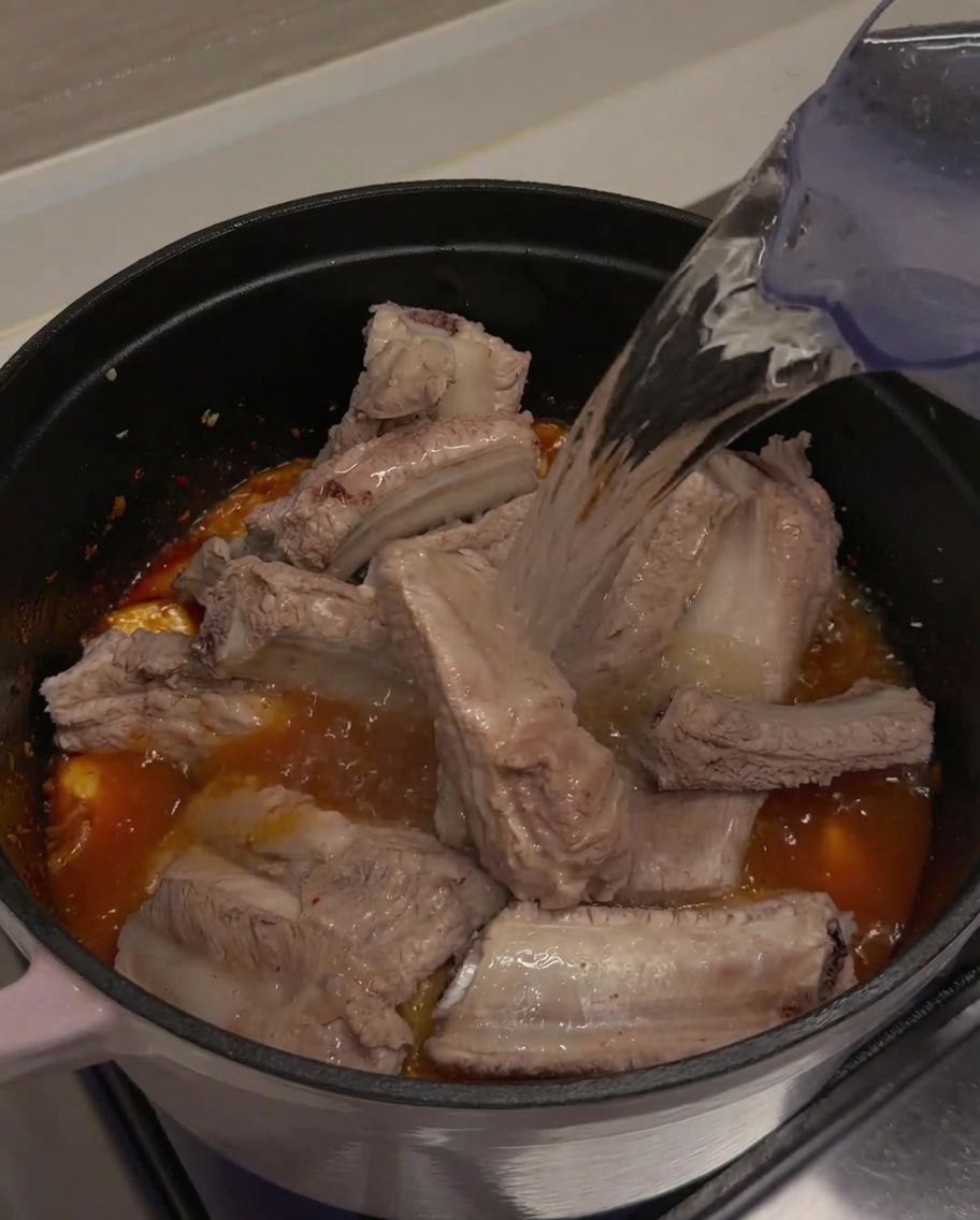 돼지갈비와 김치가 완전히 잠기도록 냄비에 맑은 물을 붓는 모습.