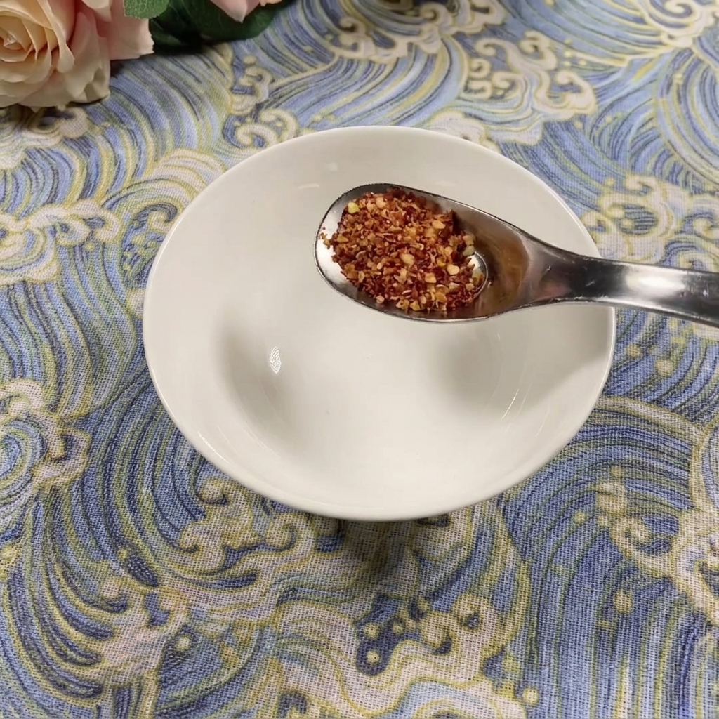 파란색 무늬가 있는 바닥 위로 빈 흰색 볼에 굵은 고춧가루 한 숟가락을 넣는 모습.