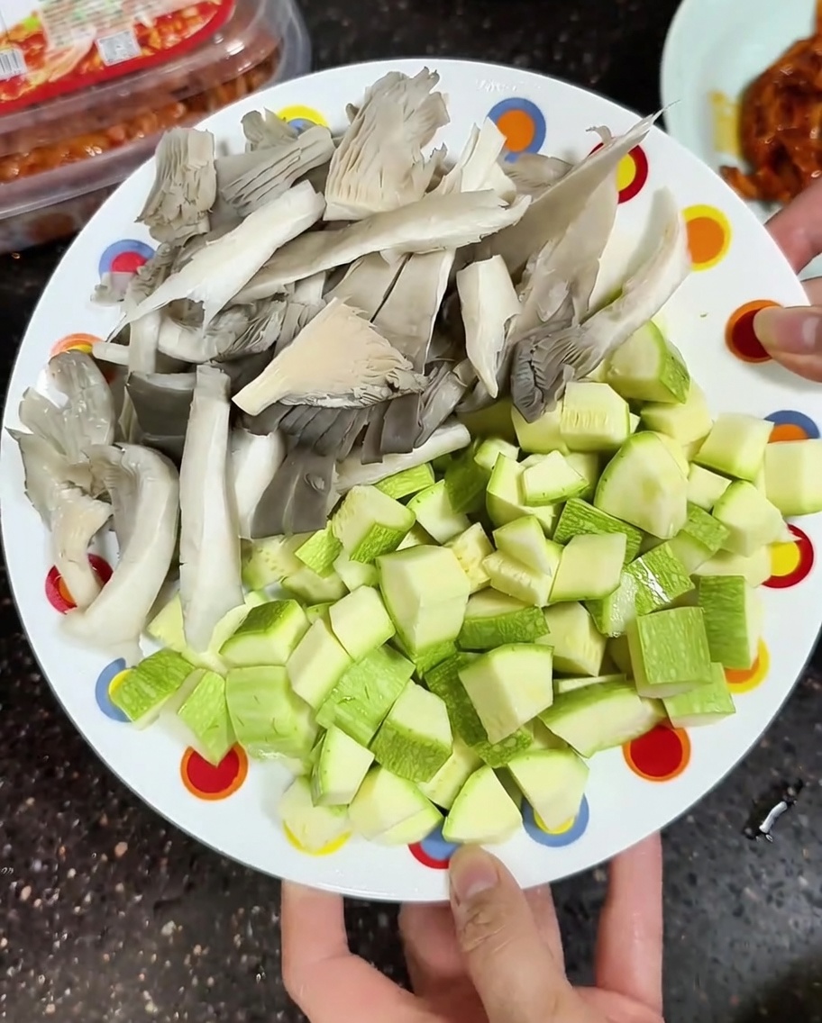 조리할 준비가 된 신선한 느타리버섯과 깍둑썰기한 애호박이 담긴 접시.