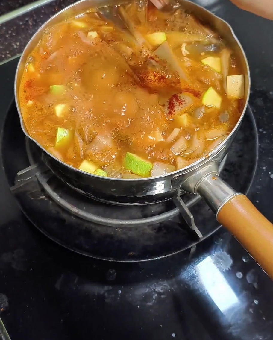 애호박과 버섯이 들어간 끓는 된장찌개 냄비에 붉은 파프리카 가루를 뿌리는 모습.
