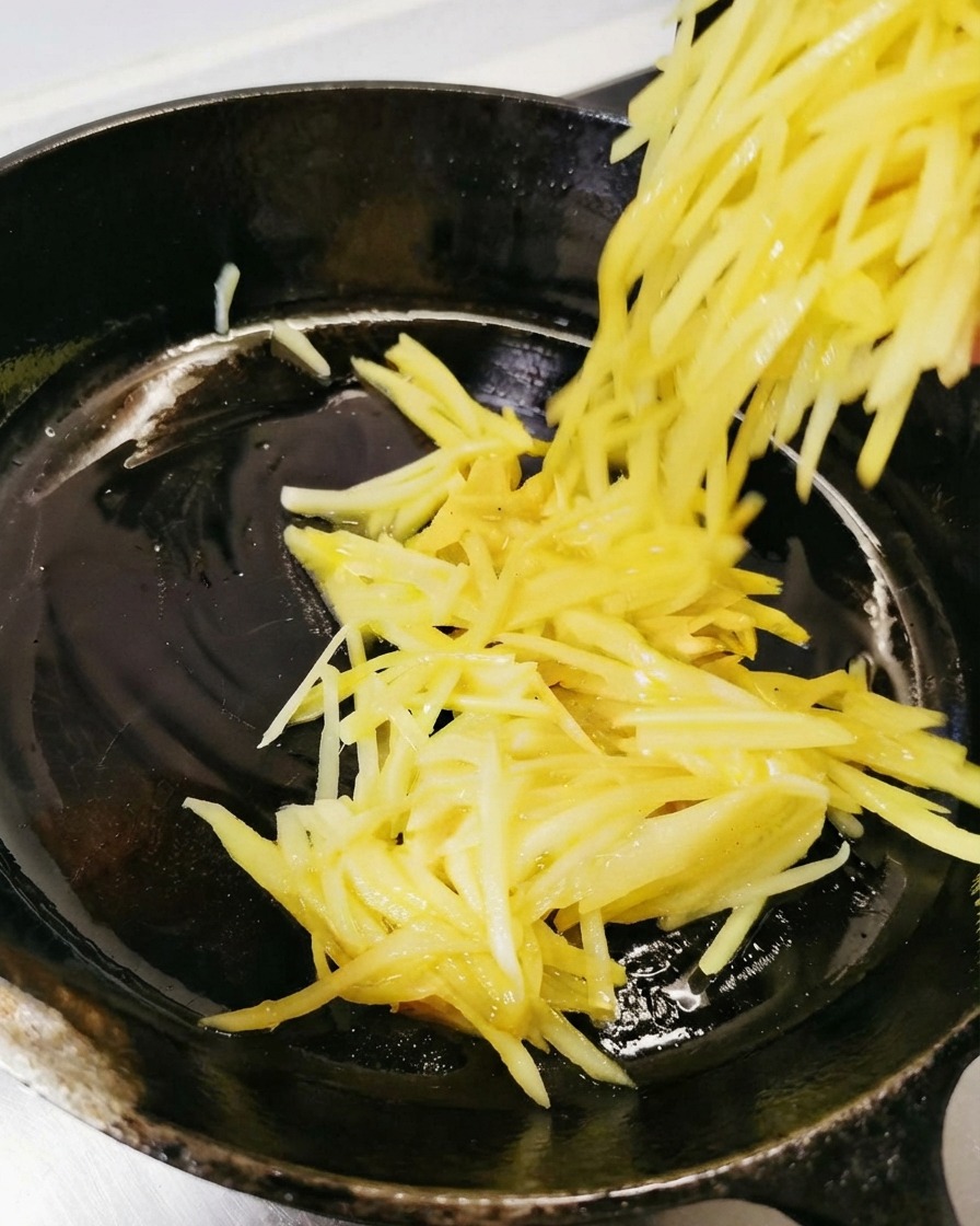 기름칠한 검은색 스킬렛 안으로 채 썬 감자 반죽이 부어져 펼쳐지는 모습.