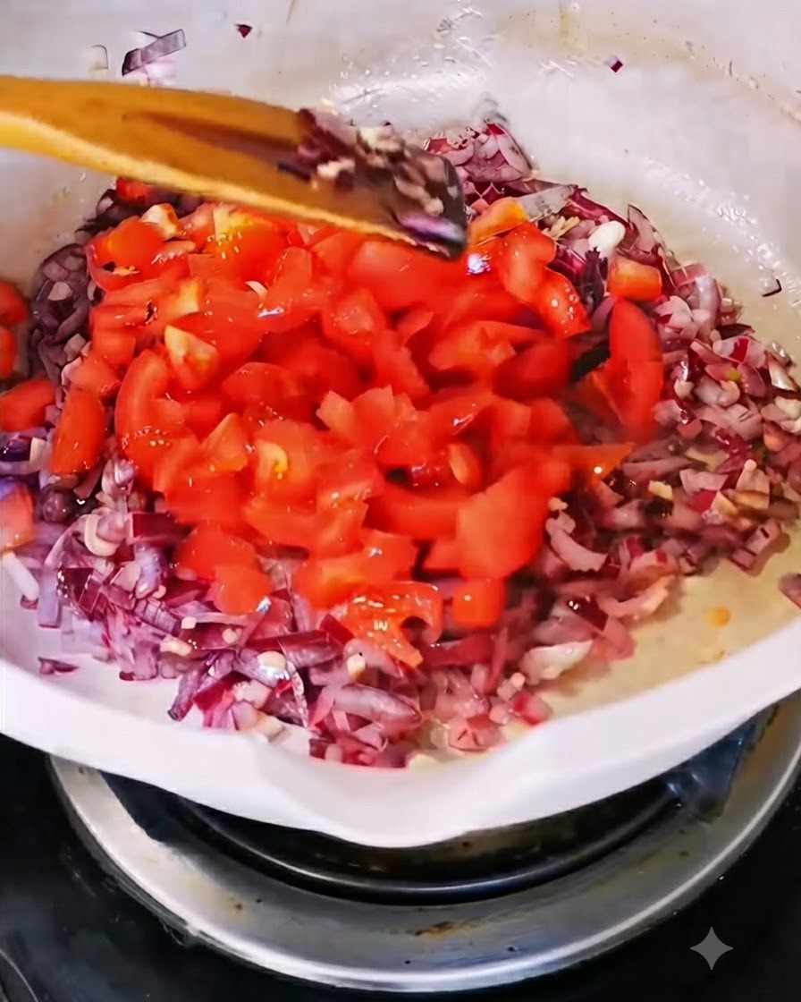 양파와 마늘을 볶고 있는 흰색 팬에 갓 다진 붉은 토마토를 넣는 모습.