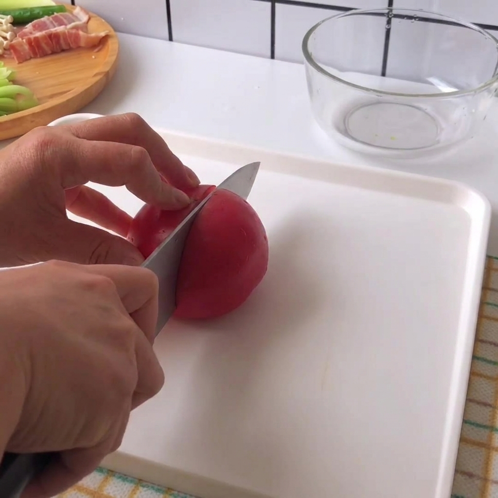 하얀 도마 위에서 칼을 들고 신선한 빨간 토마토를 한입 크기로 썰고 있는 손.