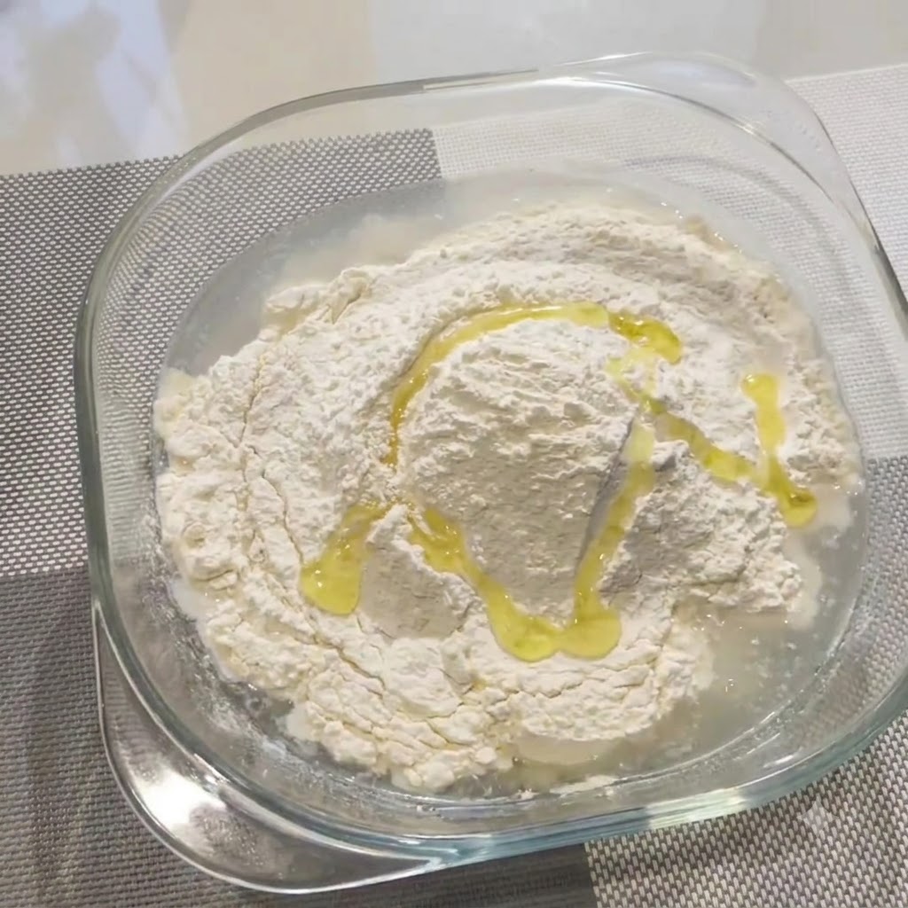 유리 볼 안의 밀가루와 물 혼합물 위에 올리브 오일을 두르는 모습.