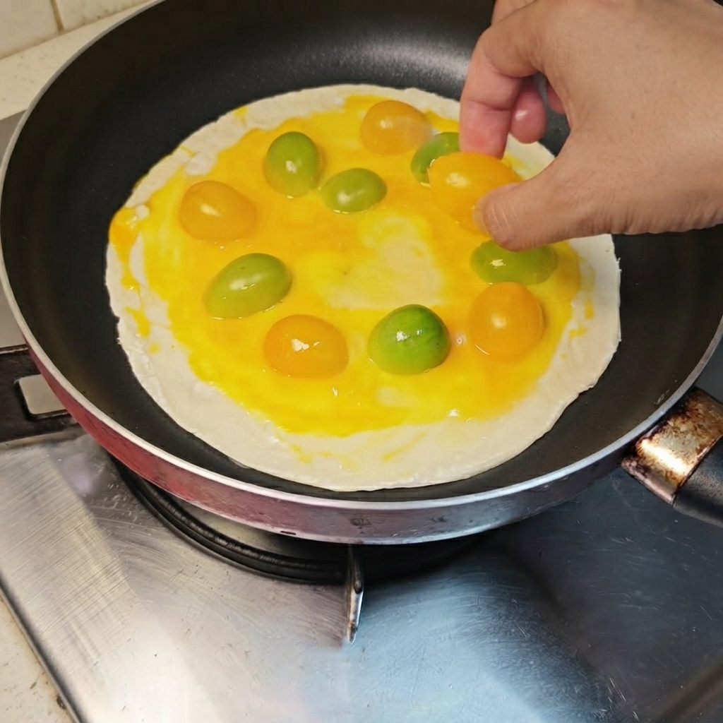 계란이 덮인 파전 위에 노란색과 주황색 방울토마토를 둥글게 배열하는 모습.