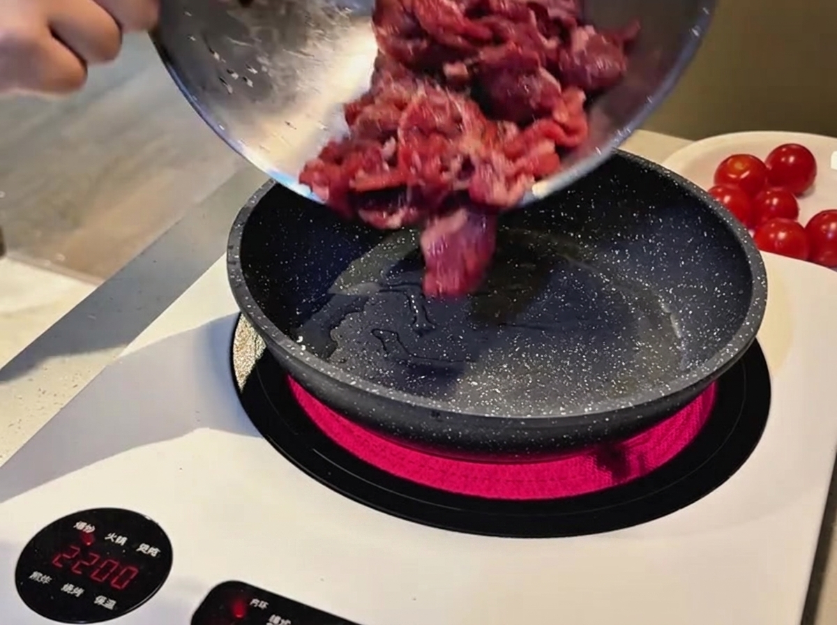 인덕션 위의 달궈진 무늬 프라이팬에 금속 볼에 담긴 마리네이드 된 생 소고기 슬라이스를 붓는 모습.
