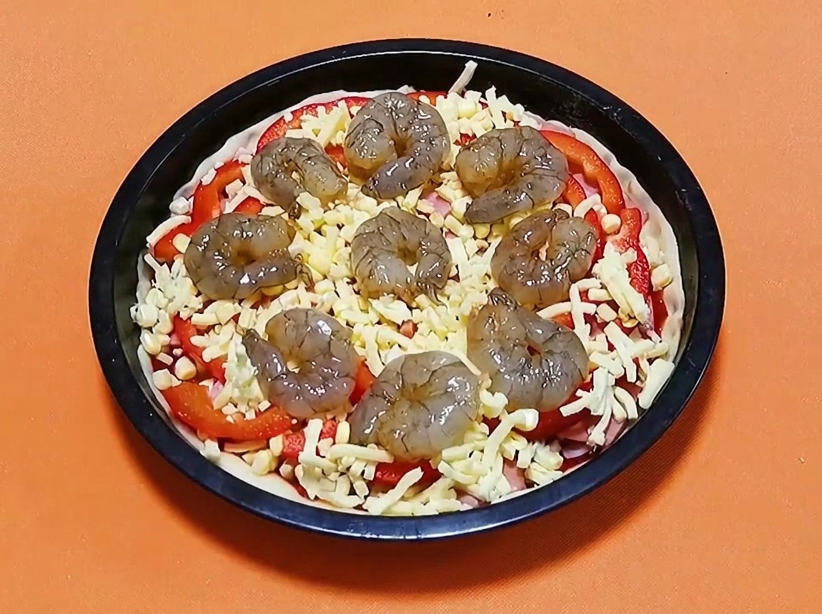 치즈, 피망, 햄이 올라간 피자 위에 생 양념 새우가 원형으로 배열되어 있는 모습.