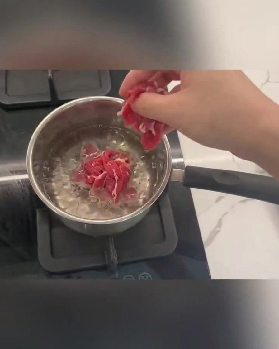 표면에 거품이 오르는 끓는 물에서 소고기 슬라이스가 익어가고 있습니다.