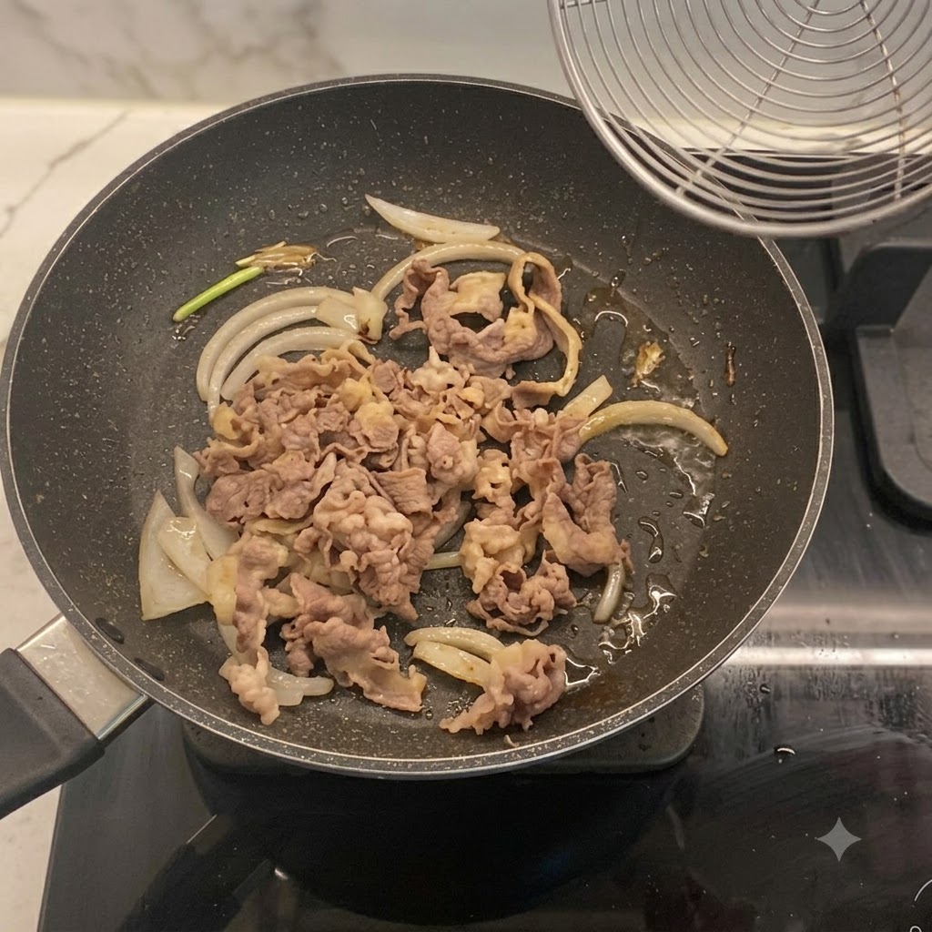 볶아진 양파와 데친 소고기 슬라이스가 프라이팬에서 섞이고 있습니다.