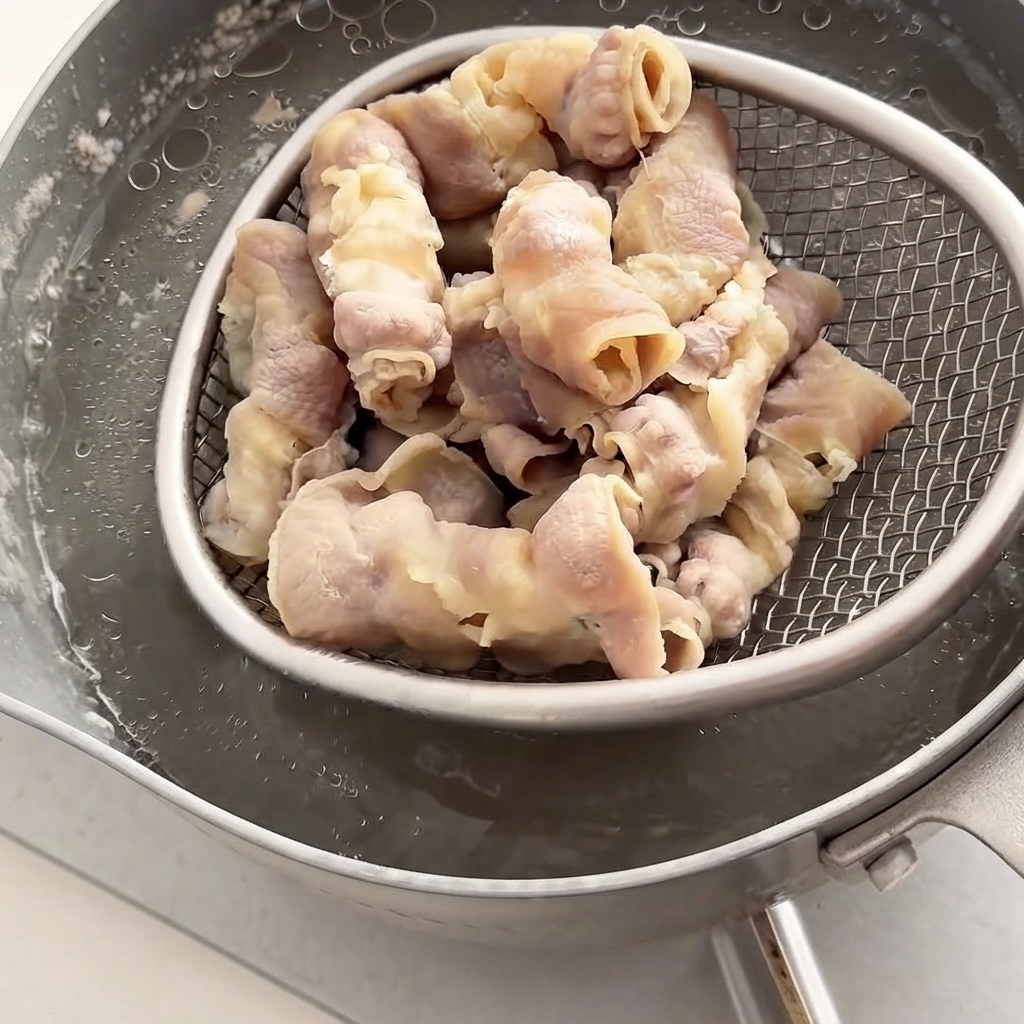 철망 체반이 뜨거운 물에서 살짝 데쳐진 소고기 롤을 건져 올리는 모습.