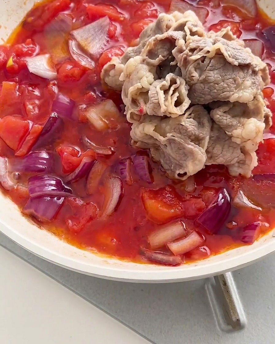 빨간 토마토와 양파가 끓고 있는 팬 중앙에 데친 소고기 롤 무더기가 추가된 모습.
