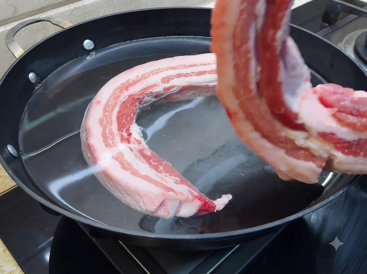 차가운 물이 채워진 큰 냄비에 생삼겹살 한 조각이 잠기는 모습.