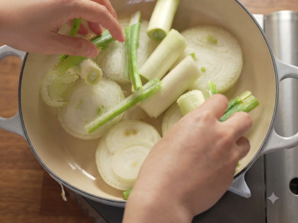 두꺼운 더중 오븐(Dutch Oven) 냄비 안에 썬 양파, 대파, 사과가 깔끔하게 배열된 모습.
