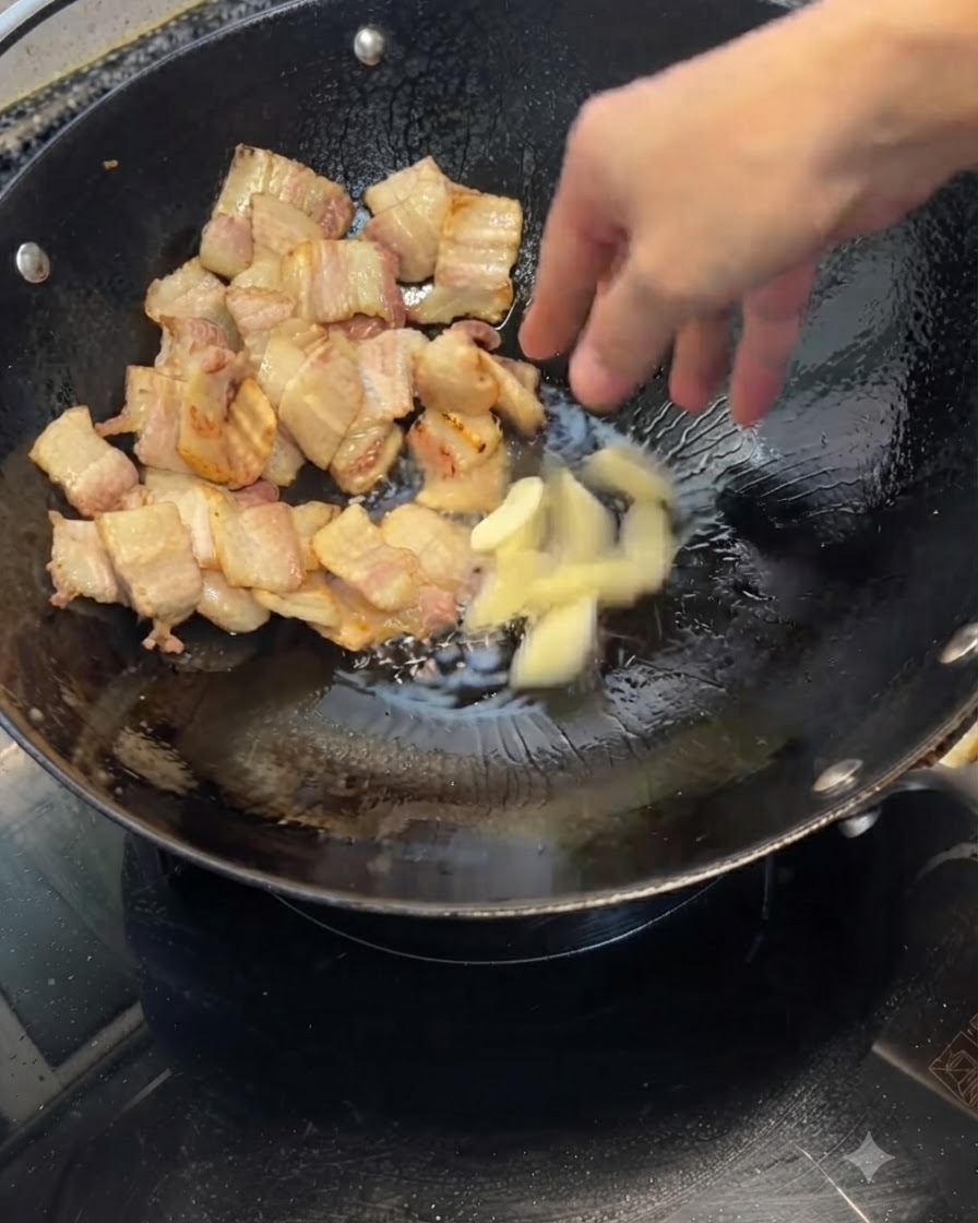 노릇하게 구워진 삼겹살이 담긴 웍에 으깬 마늘을 넣는 모습.