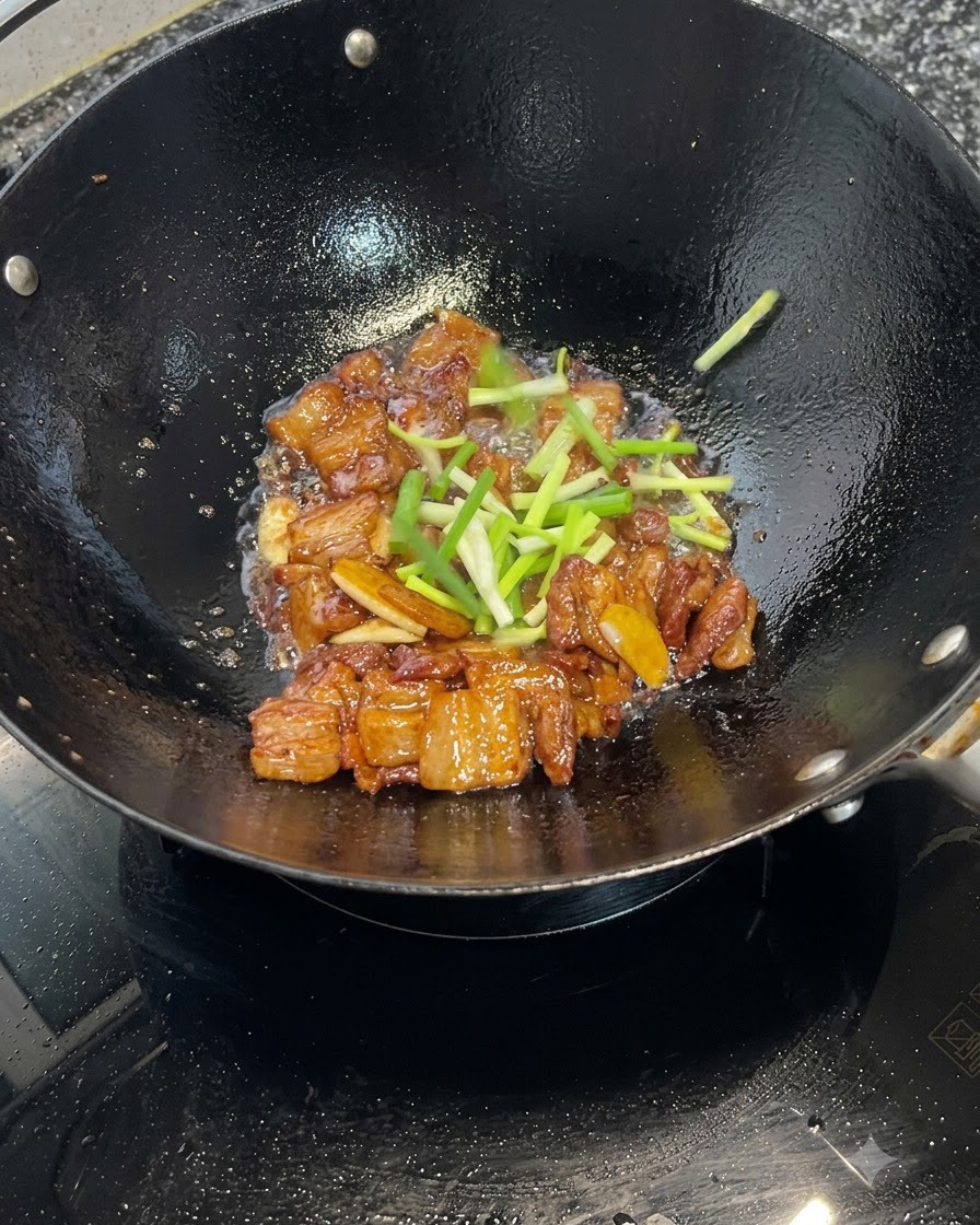웍에서 졸여지는 캐러멜라이징된 삼겹살 위에 신선한 대파를 골고루 흩뿌리는 모습.