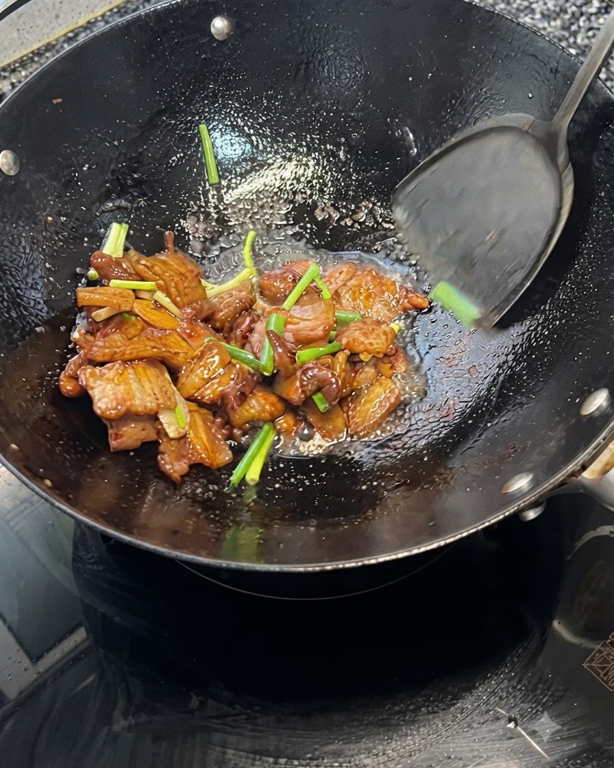 뜨거운 웍 안에서 뒤집개로 삼겹살과 대파를 함께 섞어주는 모습.