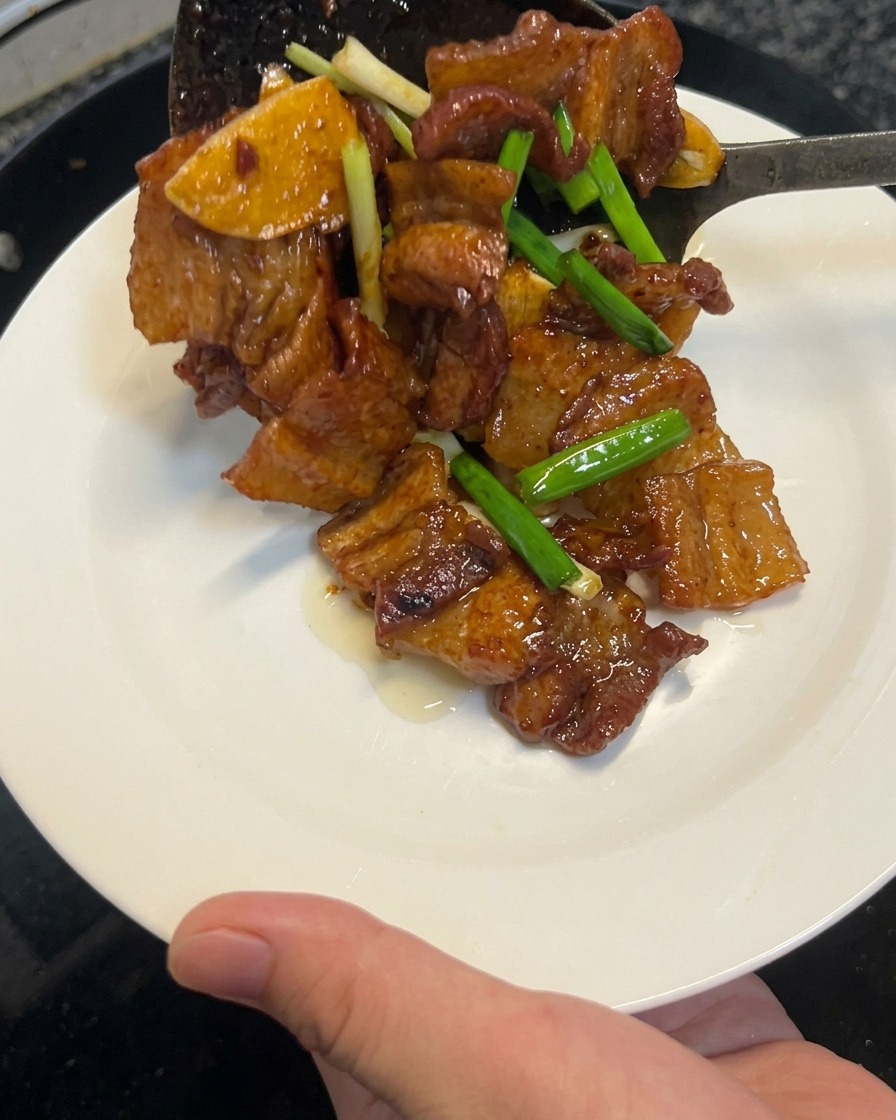 커다란 뒤집개를 이용해 다 조리된 간장 삼겹살볶음을 웍에서 깨끗한 하얀 접시로 옮겨 담는 모습.