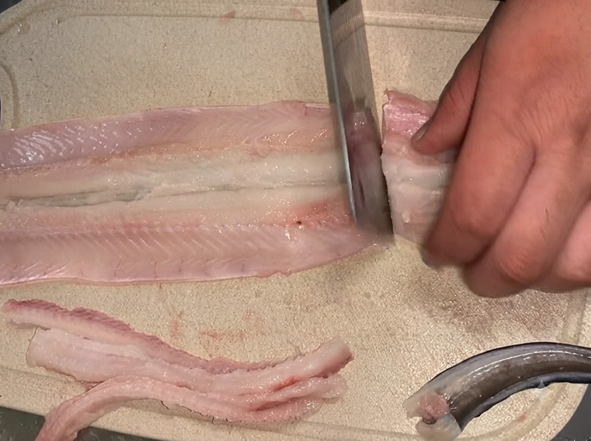 도마 위에서 뼈를 발라낸 생장어 필렛을 두 개의 섹션으로 자르는 칼.