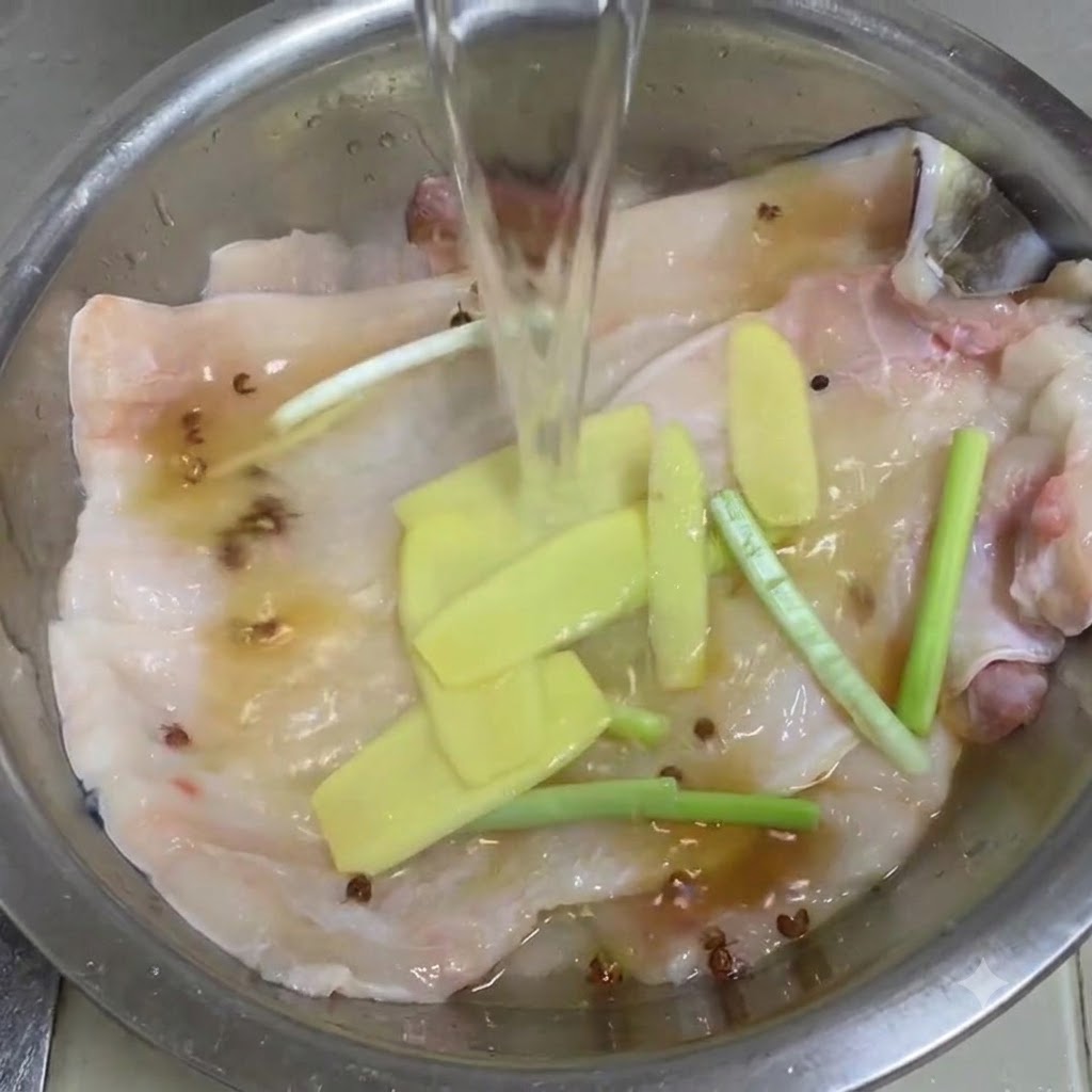 장어 필렛, 생강, 대파, 산초알이 담긴 금속 볼에 맑은 물을 붓는 모습.