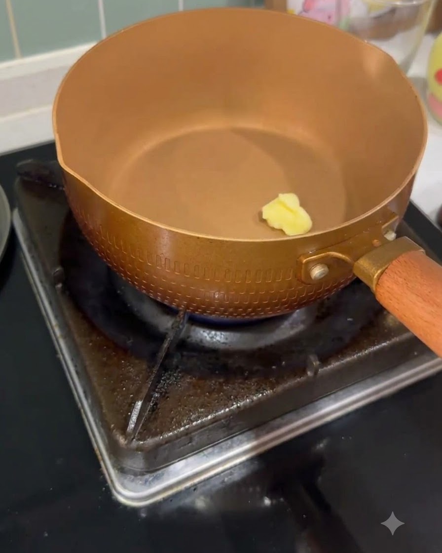 가스 불 위의 달궈진 구리빛 팬 안에서 작은 버터 조각이 완전히 녹고 있는 모습